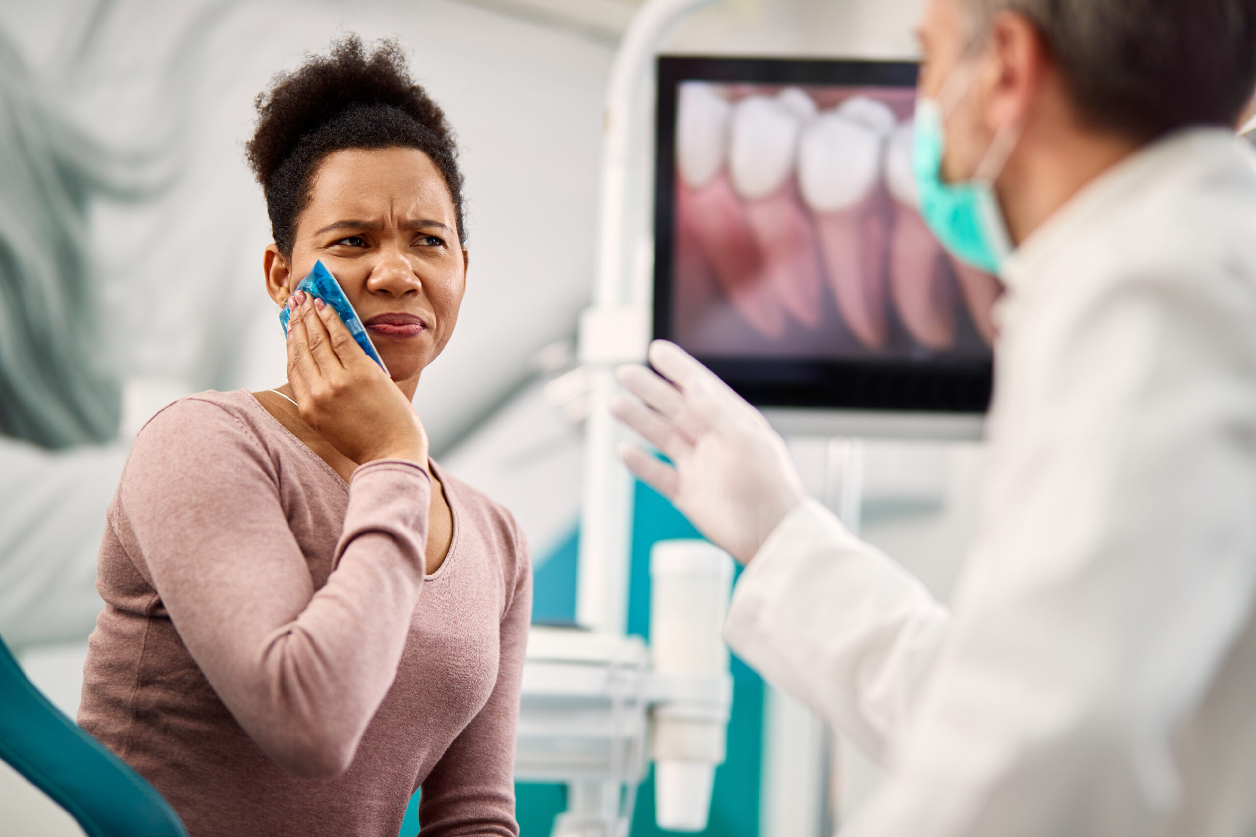 A woman in pain learning about sensitive teeth from her dentist.